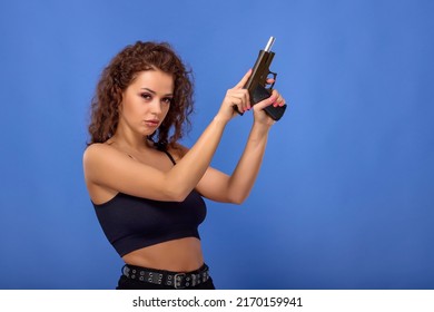 beautiful young woman with curly hair with a gun on a blue background