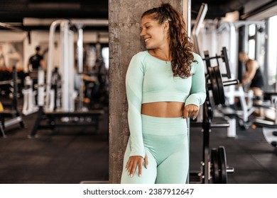 Beautiful young woman with curly hair smile and pose on sportswear in gym before exercise - Powered by Shutterstock