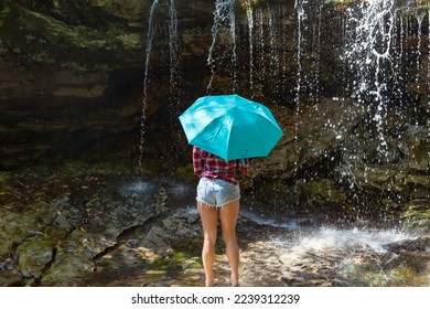 Beautiful young woman in cut-off jean shorts poses with a turquoise umbrella under a waterfall on Big Run Creek in Tucker County, WV 