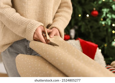 Beautiful young woman cutting wrapping paper while packing Christmas gift box on table at home, closeup - Powered by Shutterstock