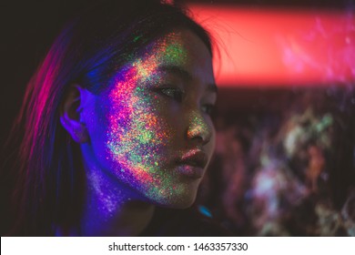 Beautiful young woman dancing and making party with fluorescent painting on her face. Neon facial portraits
