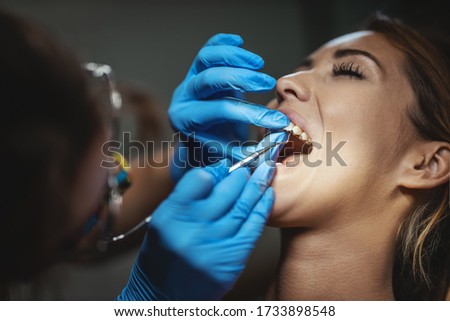 The beautiful young woman is at the dentist. She sits in the dentist's chair and the dentist sets braces on her teeth putting aesthetic self-aligning lingual locks.