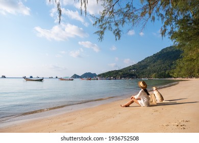 A beautiful young woman and a dog sitting on the beach together - Powered by Shutterstock