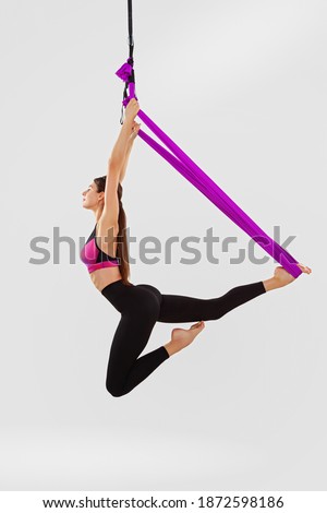 Beautiful young woman doing aerial yoga on a white background. Flying, stretching, balance, exercise and a healthy lifestyle.