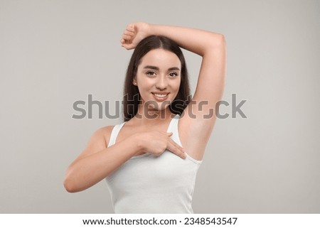 Beautiful young woman doing breast self-examination on light grey background