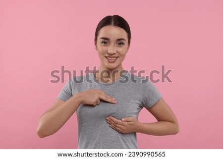 Beautiful young woman doing breast self-examination on pink background