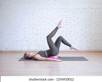 Beautiful young woman doing pilates workout with small pink fitness ball, leg arch exercise. Indoor, loft background, toned blue. Wellness, recovery, rehabilitation, prevention spine desease, smart - Powered by Shutterstock