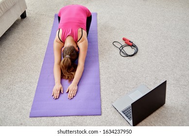 Beautiful Young Woman Doing Stretching Exercise On Floor At Home, Online Training On Laptop Computer, Copy Space. Full Length Portrait. Yoga, Pilates, Working Out Exercising