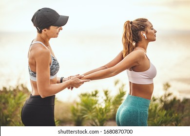 A beautiful young woman is doing stretching exercise at the sea beach in summer sunny day supported by her friend. - Shutterstock ID 1680870700