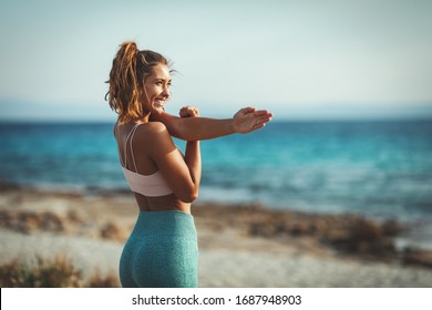 A Beautiful Young Woman Is Doing Stretching Exercise At The Sea Beach In Summer Sunny Day.