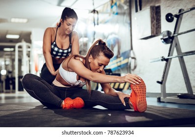 Beautiful Young Woman Doing Stretching Exercise With A Female Personal Trainer At The Gym.