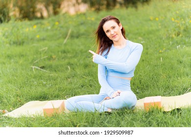 Beautiful young woman doing yoga in a park at sunset in spring or summer pointing with the finger. yoga instructor concept. yoga class. commercial yoga. copy space