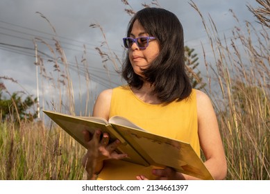 Beautiful young woman with down syndrome, trisomy 21 reading a book outdoors. Calm landscape.