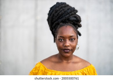 Beautiful young woman with dreadlocks in front of gray wall
