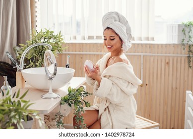 A Beautiful Young Woman Dressed In A Bathrobe Makes Her Own Make-up In The Bathroom. Concept Of Beauty And Make-up.