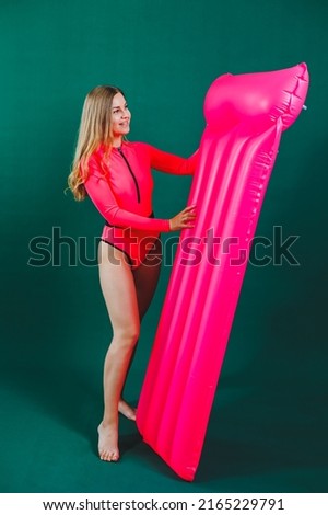 Beautiful young woman dressed in a pink swimsuit posing while standing with an air mattress over isolated background. Inflatable pink mattress