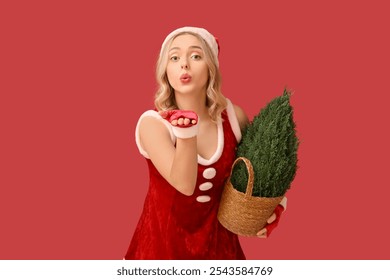 Beautiful young woman dressed as Santa Claus with Cypress tree blowing kiss on red background - Powered by Shutterstock