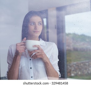 Beautiful Young Woman Drink First Morning Coffee At Modern Home Interior With Rain Drops On Big Window Door Glass