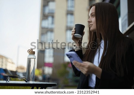 Beautiful young woman drinking coffee and browsing a mobile phone in a outdoor cafe. Portrait of a pretty female person with long brown hair relaxing on a coffee break