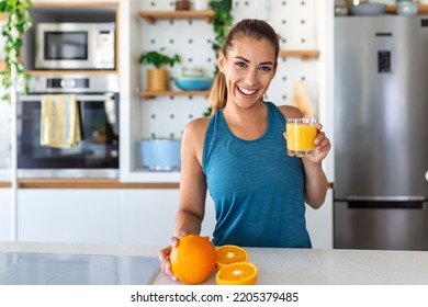 Beautiful young woman drinking fresh orange juice in kitchen. Healthy diet. Happy young woman with glass of juice and orange at table in kitchen. - Shutterstock ID 2205379485