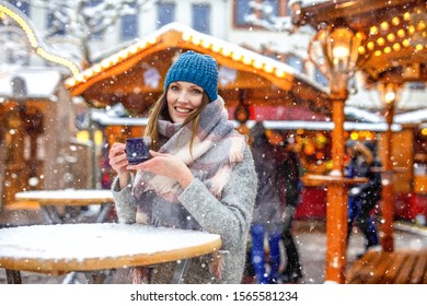 Beautiful young woman drinking hot punch, mulled wine on German Christmas market. Happy girl in winter clothes with lights on background on winter snow day in Dresden, Germany. - Powered by Shutterstock