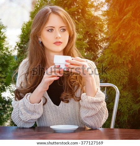 Beautiful young woman drinking hot coffee or tea in the morning at restaurant. Lifestyle photo, girl enjoying her morning coffee in summer garden