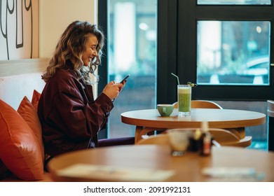 Beautiful young woman drinking matcha latte coffee and using smartphone in a cafe - Powered by Shutterstock