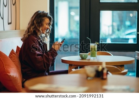 Beautiful young woman drinking matcha latte coffee and using smartphone in a cafe