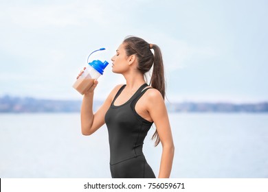 Beautiful Young Woman Drinking Protein Shake On River Bank