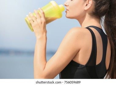 Beautiful Young Woman Drinking Protein Shake On River Bank