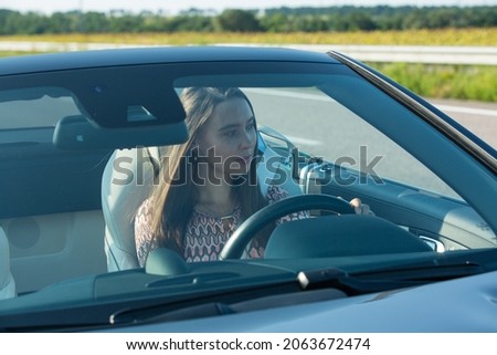 Beautiful young woman driving a Mercedes Benz SL550 convertible on the road. The girl is very attentive and focused while driving.