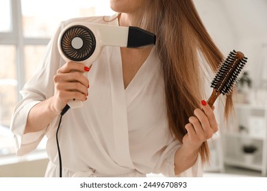 Beautiful young woman drying her hair with round brush in bathroom, closeup - Powered by Shutterstock