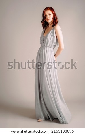 Beautiful young woman in dust blue dress. Studio portrait of ginger lady in evening gown dancing on high heel shoes in studio. Bridesmaid's outfit for hen party.
