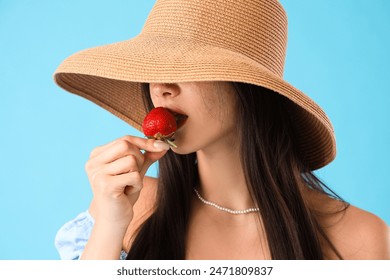 Beautiful young woman eating fresh strawberry on blue background - Powered by Shutterstock