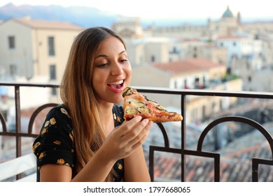 Beautiful young woman eating a slice of vegetarian pizza at sunset on terrace in Palermo, Italy