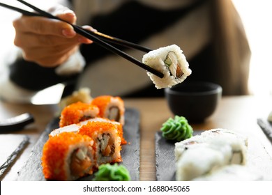 Beautiful young woman eating sushi roll at cafe. Woman eating sushi set with chopsticks on restaurant.