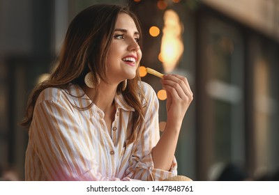 Beautiful Young Woman Eating Tasty French Fries Outdoors