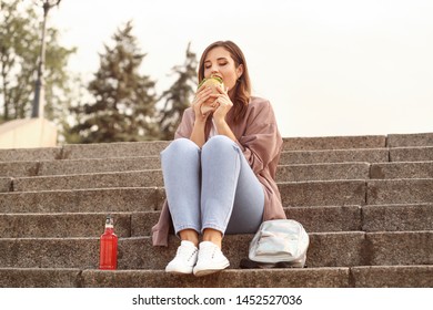 Beautiful Young Woman Eating Tasty Burger Outdoors