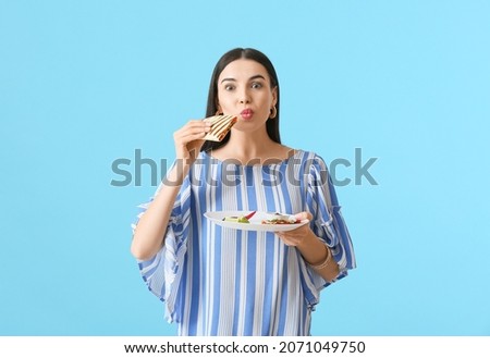 Beautiful young woman eating tasty quesadilla on color background