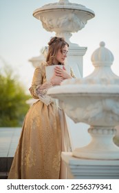 A beautiful young woman in an eighteenth century historical gold dress stands on the stairs of a mansion with a book in her hands. the princess is reading in the palace. fabulous image - Shutterstock ID 2256379341
