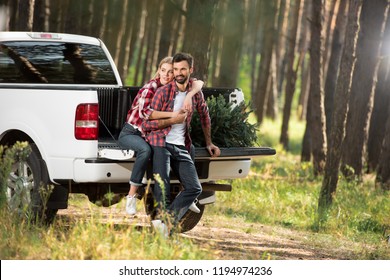 beautiful young woman embracing boyfriend from behind while sitting in car trunk with christmas tree in forest - Shutterstock ID 1194974236