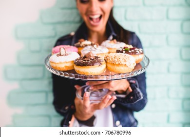 Beautiful young woman enjoying in delicious glazed and decorated donuts. Selective focus on front donut.
