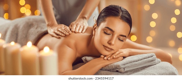 Beautiful young woman enjoying massage in spa salon. Relaxed brunette girl lying on massage bed with closed eyes during spa treatment procedure. Beauty treatment, skin care, wellbeing