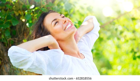 Beautiful Young Woman Enjoying Nature Outdoor. Happy And Healthy Smiling Brunette Girl With Healthy Smile Relaxing In The Summer Park. Breathing Fresh Air. Sunny Day. Health Care Concept