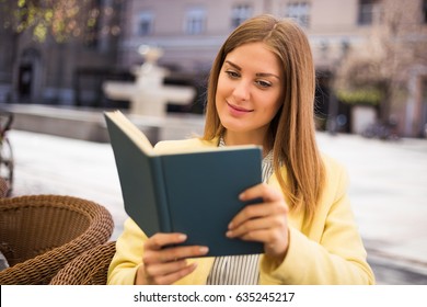 Beautiful young woman enjoys reading book at the cafe.Leisure time at the city