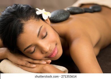 Beautiful young woman with eyes closed receiving hot stone massage at salon spa