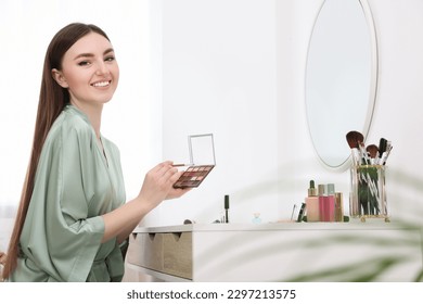 Beautiful young woman with eyeshadow palette and brush at dressing table indoors - Powered by Shutterstock