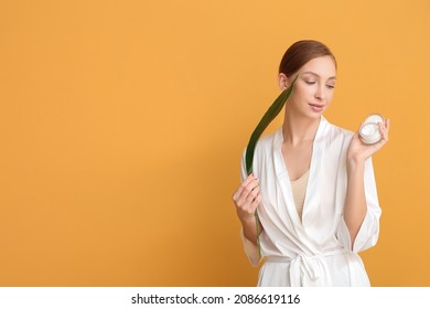 Beautiful Young Woman With Facial Cream And Tropical Leaf On Color Background