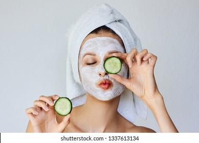 Beautiful young woman with facial mask on her face holding slices of fresh cucumber. Skin care and treatment, spa, natural beauty and cosmetology concept, over white background - Powered by Shutterstock