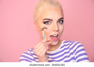 Beautiful young woman with fake eyelashes on pink background